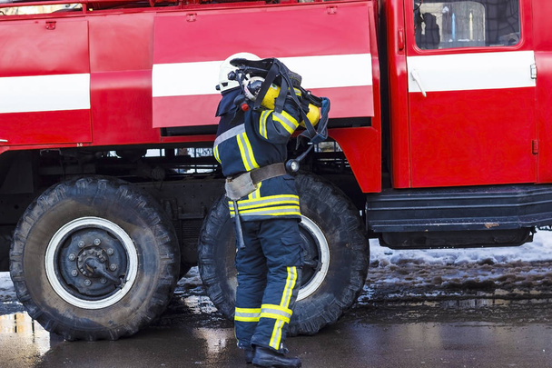 A fireman standing near a red fire engine and holding an oxygen  - Фото, зображення
