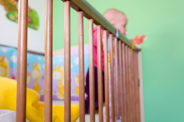 Baby standing in a crib and holding side of the bed. - Фото, изображение