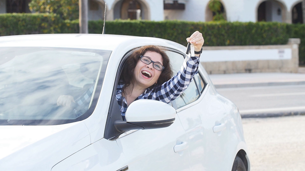 Onnellinen nainen näyttää uuden auton avaimen ulkona
 - Materiaali, video