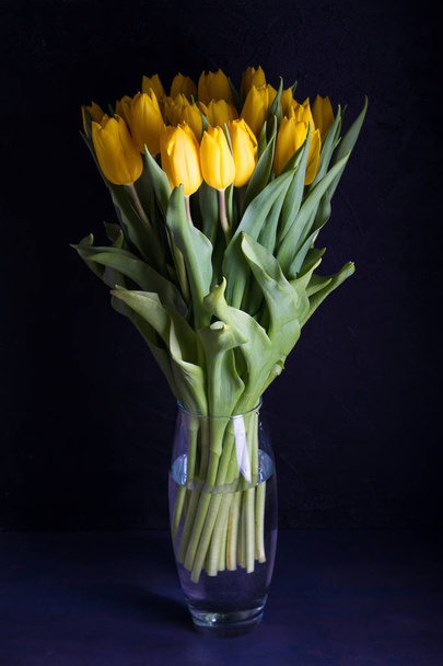 Bouquet of spring tulips flowers in vase on black  background. Yellow tulips  - Foto, Bild