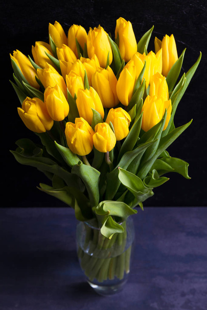 Bouquet of spring tulips flowers in vase on black  background. Yellow tulips  - Foto, immagini