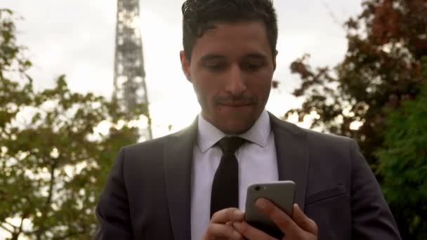 Man in a suit using application on a smartphone next to the Eiffel Tower - Filmati, video