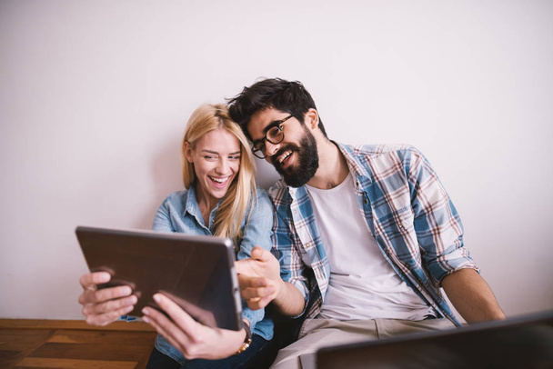 счастливая молодая влюбленная пара, делающая интернет-звонок на планшетном компьютере сидя на полу
 - Фото, изображение