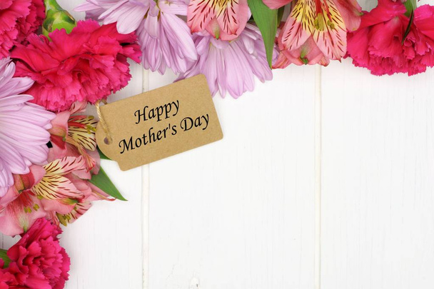 Ετικέτα δώρο ημέρα της μητέρας ανάμεσα σε ένα περίγραμμα γωνία ροζ λουλούδια πάνω σε ένα λευκό φόντο ξύλου - Φωτογραφία, εικόνα