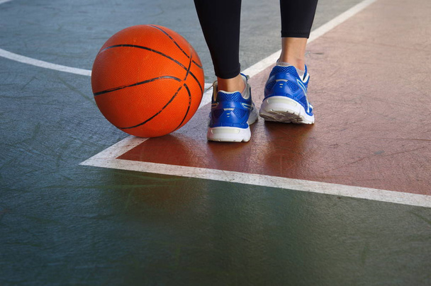 orange basketball on gymnasium floor with woman legs wear sport  - Fotoğraf, Görsel