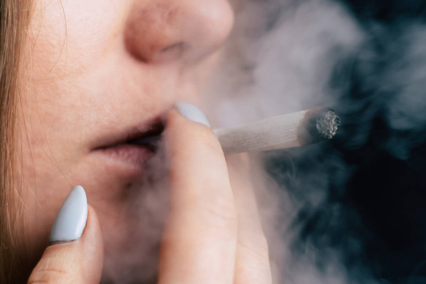 Une femme fume de l'herbe de cannabis, un joint et un briquet dans ses mains. Fumée sur fond noir. Concepts de la consommation de marijuana médicale et légalisation du cannabis
. - Photo, image