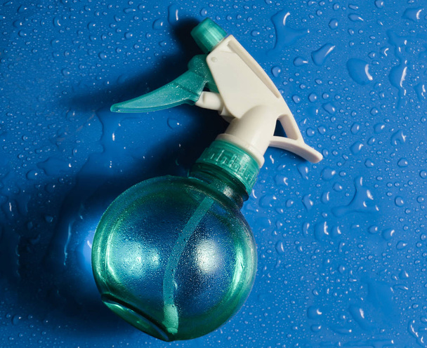 Una botella de spray en gotas de agua sobre un fondo azul. Vista superior
. - Foto, imagen