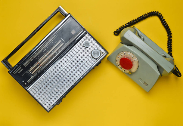 Cultura de los años 70. Receptor de radio y teléfono giratorio sobre fondo amarillo. Dispositivos retro. Vista superior
. - Foto, imagen