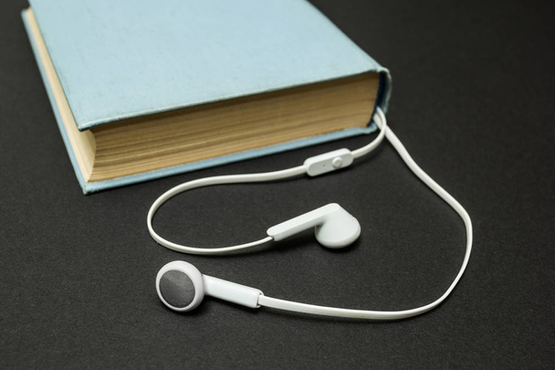 Old blue book, and white headphones on a black background - Фото, зображення
