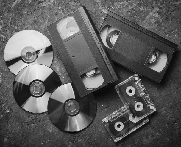 A 90-es évek szórakoztatás és a média technológia. CD-k, audio kazetták, videokazetták, fekete beton felületre. Szemközti nézet. - Fotó, kép