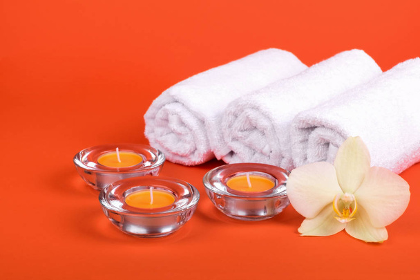 Towels, candles and orchid flowers for a spa relaxation on orange background - Fotó, kép