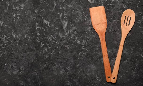 A wooden spatula and a spoon for cooking on a black concrete table. Space for text. Top view - Foto, immagini