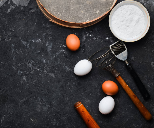  Ingrediënten voor pasta. Het kookproces. Eieren, meel, keukengerei op een zwarte betonnen tafel. Hulpmiddelen voor het koken. Italiaanse keuken. Bovenaanzicht. Plat leggen.  - Foto, afbeelding