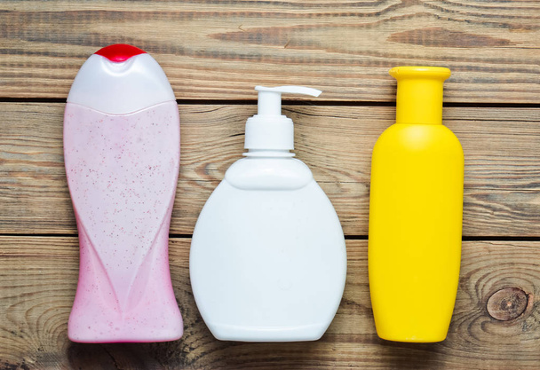 Flaschen mit Produkten für das Badezimmer. Duschgel, Flüssigseife, Shampoo auf einem Holztisch. Ansicht von oben. - Foto, Bild