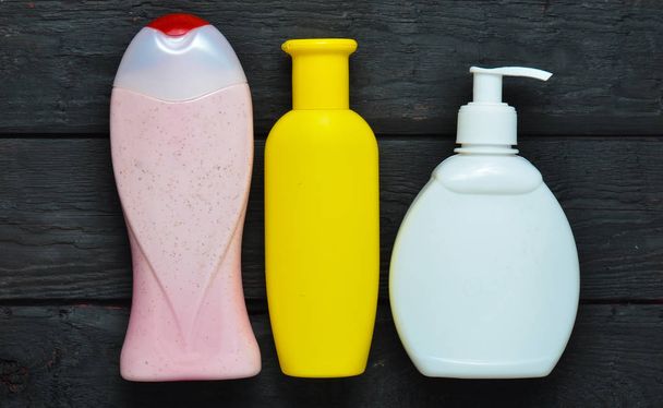 Flaschen mit Produkten für die Dusche. Duschgel, Flüssigseife, Shampoo auf einem schwarzen Holztisch. Ansicht von oben. - Foto, Bild