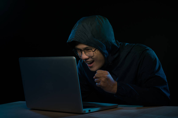 Hacker in een donkere hoody zit van een notebook. Computer privacy aanval - Foto, afbeelding