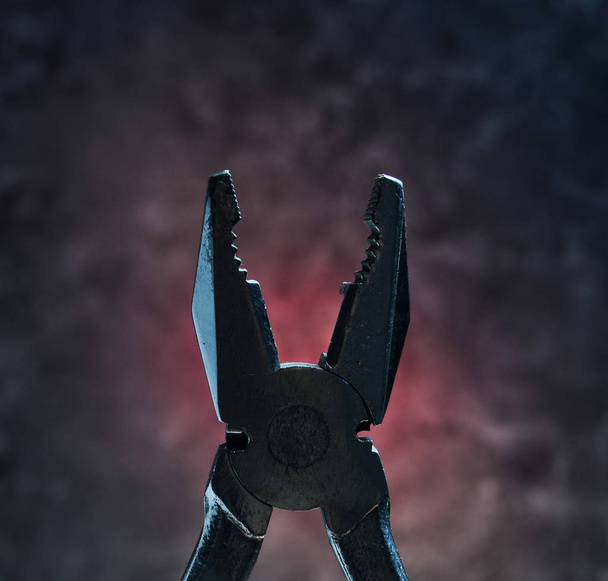 Silhouette of the pliers against the background of the concrete wall. Work tool. Mystical red light. - Photo, Image
