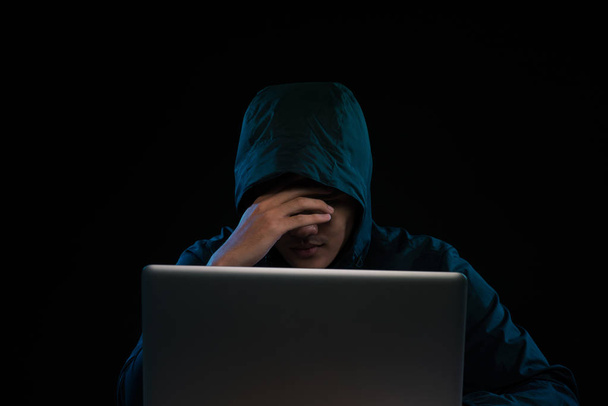 Hacker in een donkere hoody zit van een notebook. Computer privacy aanval - Foto, afbeelding