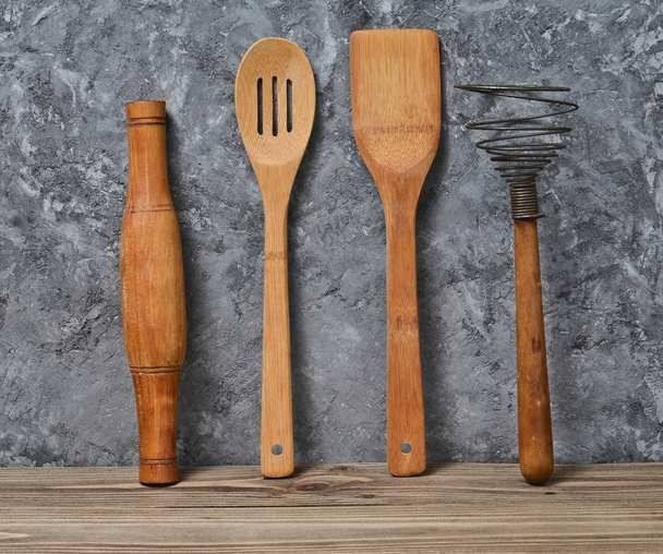 Wooden tools for the rattles against the gray concrete wall. Wooden spatula, spoon, whisk, rolling pin. - Valokuva, kuva