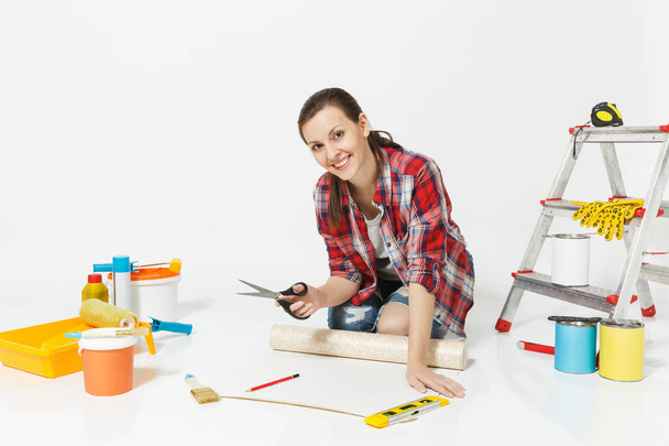 Γυναίκα συνεδρίασης με το μεγάλο ψαλίδι, μολύβι, ρολά ταπετσαρίας, όργανα για διαμέρισμα ανακαίνιση που απομονώνονται σε λευκό φόντο. Αξεσουάρ για κόλλημα, εργαλεία ζωγραφικής. Επισκευή concept home. Χώρο αντίγραφο. - Φωτογραφία, εικόνα