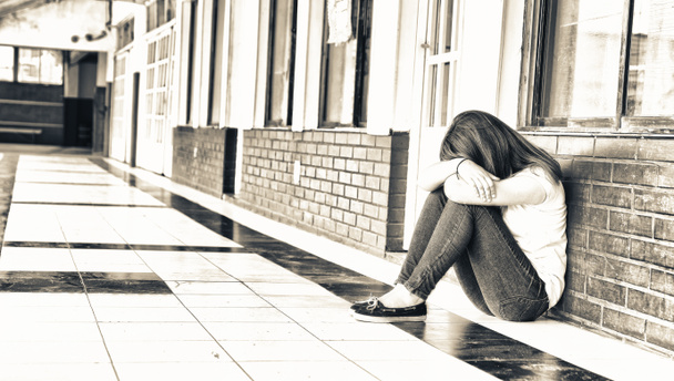 Ragazza adolescente isolata seduta disperata nel corridoio della scuola. Concetto di bullismo
. - Foto, immagini