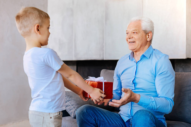Nice pleasant boy giving a present to his grandfather - Foto, imagen