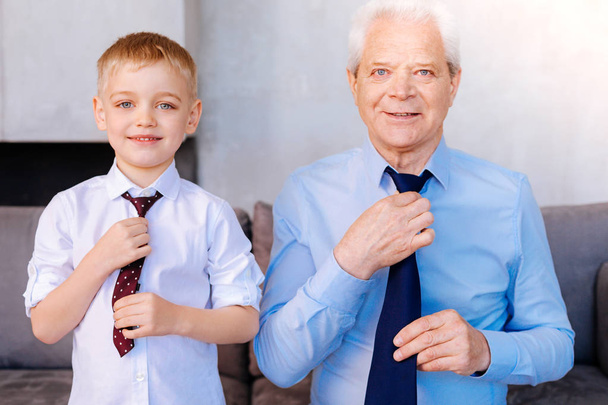 Nice cheerful grandfather and grandson fixing their ties - Фото, зображення