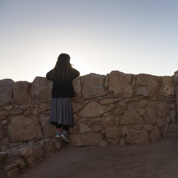 Achteraanzicht van meisje leunend tegen muur op fort, Masada, Judean Desert, dode zee regio, Israël - Foto, afbeelding