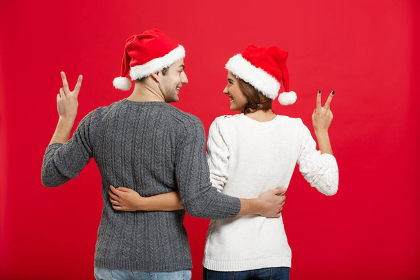 Χριστούγεννα Concept - ΠΙΣΩ ΟΨΗ του πορτρέτου όμορφη νεαρό ζευγάρι δείχνει η χειρονομία δύο δάχτυλων - Φωτογραφία, εικόνα