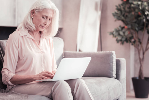 Busy aged woman sitting and using laptop. - Zdjęcie, obraz