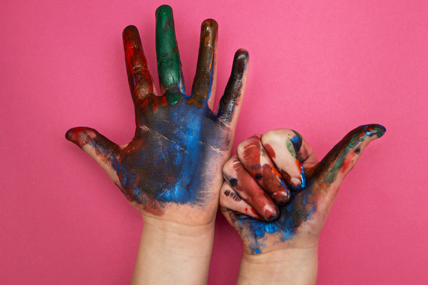 Children's hand, smeared with multicolored paint on a pink background. Thumbs up - Photo, Image