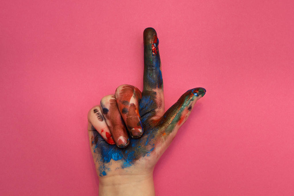 Child's hand in multicolored paint points up on a pink background. - Foto, immagini