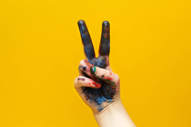 Hand in multi-colored paint, showing a sign of victory and peace close-up, isolated on a yellow background. - Фото, зображення