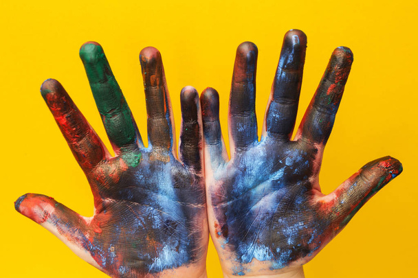 Children's hands are stained with a multicolored paint on a yellow background. - Фото, зображення