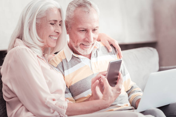 Joyful smart couple smiling and looking at the smartphone. - 写真・画像
