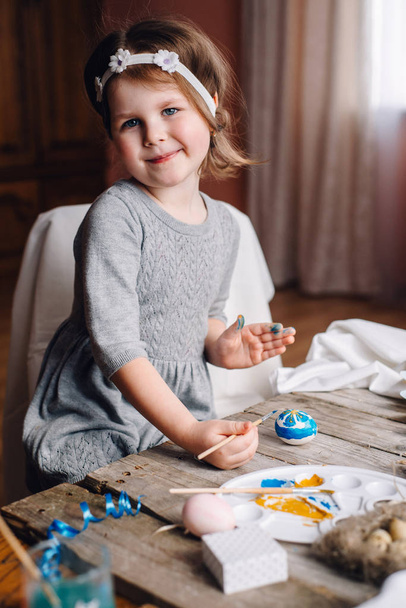 Schattig meisje kleuren ei aan houten tafel en plezier - Foto, afbeelding