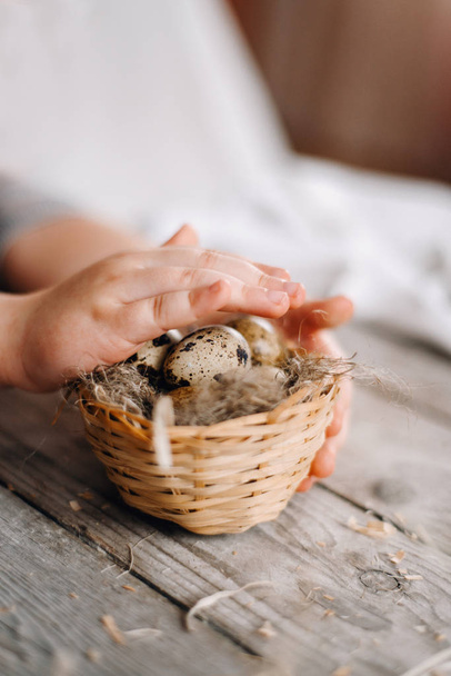 Oříznutý pohled dětské ruce drží a pokrývající hnízdo s křepelčími vejci na pozadí Dřevěná prkna - Fotografie, Obrázek