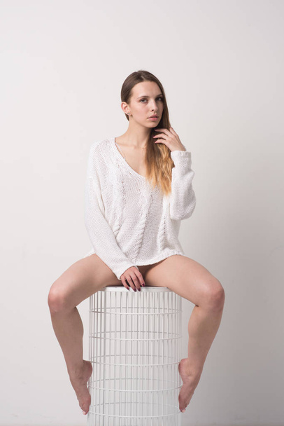 young beautiful girl posing in studio, sitting on chair in white sweater - Photo, Image