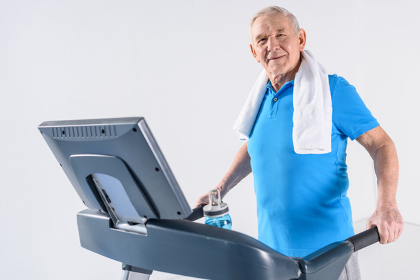 Widok z boku starszego człowieka z ręcznikiem ćwiczeń na bieżni na szarym tle - Zdjęcie, obraz