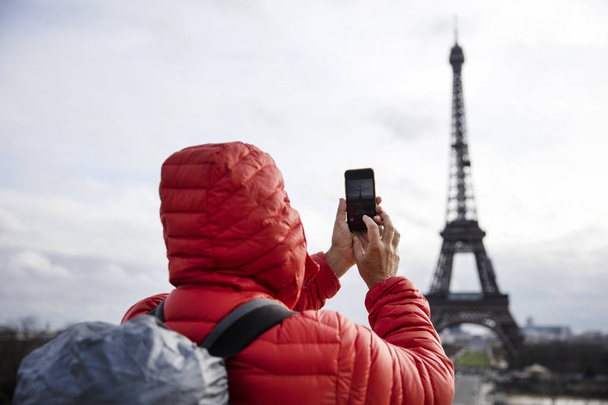 Fiatal férfi hátizsák, figyelembe véve a fotó mobiltelefonnal, az Eiffel-torony Párizs, Franciaország - Fotó, kép