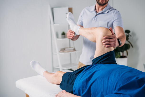 partial view of rehabilitation therapist massaging senior mans leg on massage table - Photo, Image