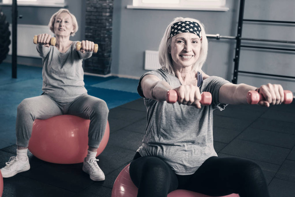 Two senior women stretching out hands with dumbbells - Foto, imagen