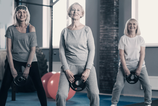 Senhoras seniores de pé com discos de peso no ginásio
 - Foto, Imagem