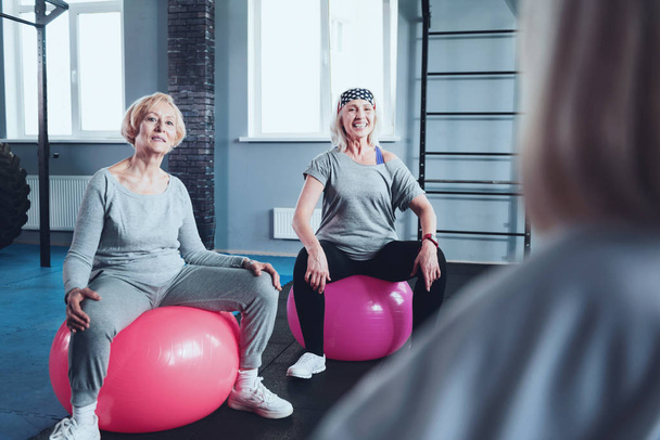 Sporty retired ladies sitting on fitness balls while training - Foto, Imagen