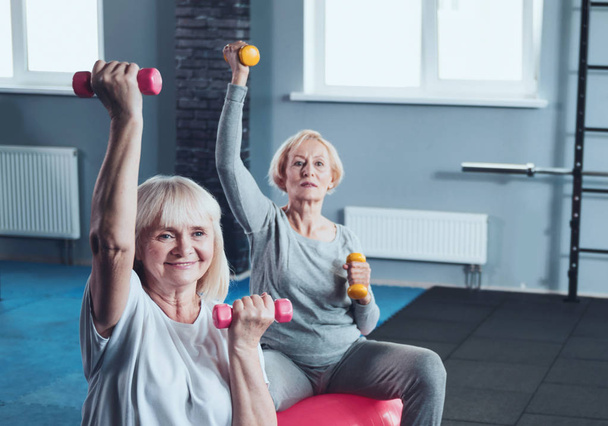 Two elderly ladies lifting weights while training in gym - Foto, immagini