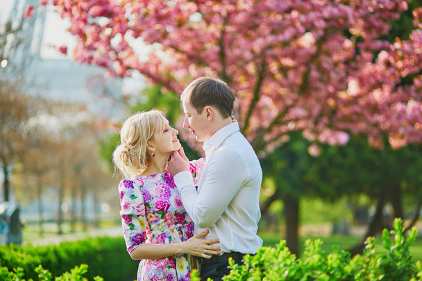 Beautiful romantic couple under blooming cherry tree on a spring day with Eiffel tower in background in Paris, France - Zdjęcie, obraz
