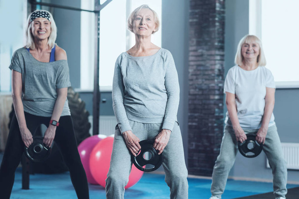 Aktive reife Frauen schwingen im Fitnessstudio die Gewichtsscheibe - Foto, Bild