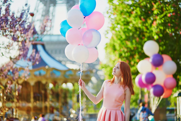 Happy young girl with bunch of pink and blue balloons in front of the Eiffel tower and merry-go-round in Paris, France - Foto, afbeelding