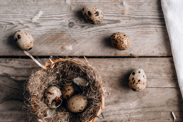 Top view of festive composition with quail eggs, nest and feathers on horizontal wooden planks background - Foto, Imagen