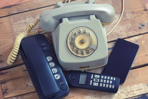 Diferentes tipos de teléfonos teléfono fijo, teléfono inteligente, teléfono con rotativo en tablero de madera
 - Foto, Imagen